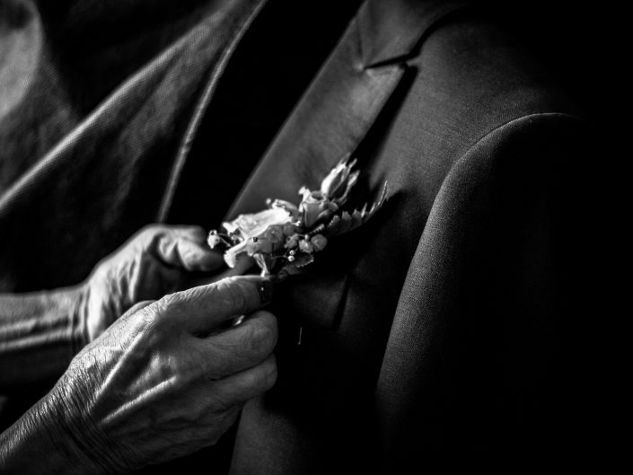 Dettagli di Matrimonio in bianco e nero. Le mani della madre dello sposo che si occupa degli ultimi ritocchi